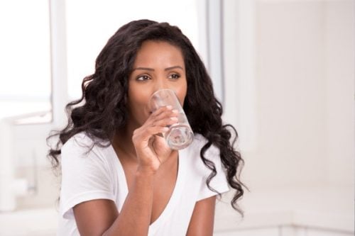 Woman drinking a glass of clear water in a bright kitchen, representing the health and wellness benefits of clean, purified water.