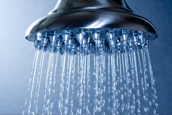 Close-up of a chrome high-pressure shower head releasing multiple streams of water against a blue background.