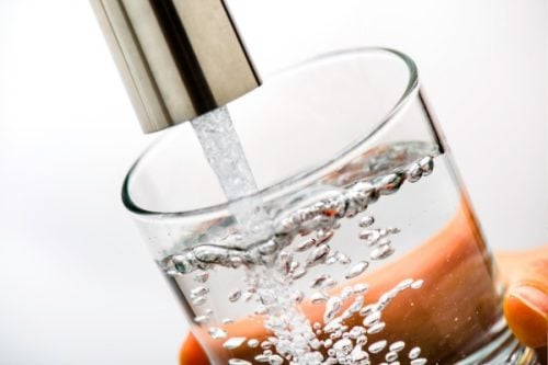 Close-up of a glass being filled with clear, fresh water from a faucet, with bubbles forming as the water pours in.