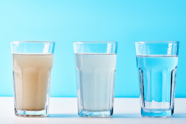 Three glasses of water showing different levels of clarity—one brown and murky, one cloudy, and one clear—illustrating water quality differences.