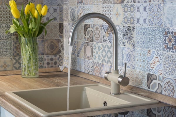 Stylish kitchen faucet with water running into beige sink with tiled backsplash.
