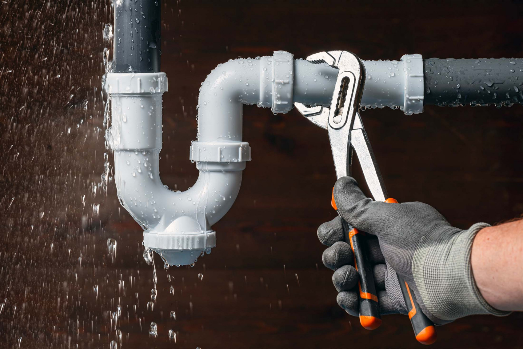 Plumber using wrench on leaking pipe with water spraying during repair.