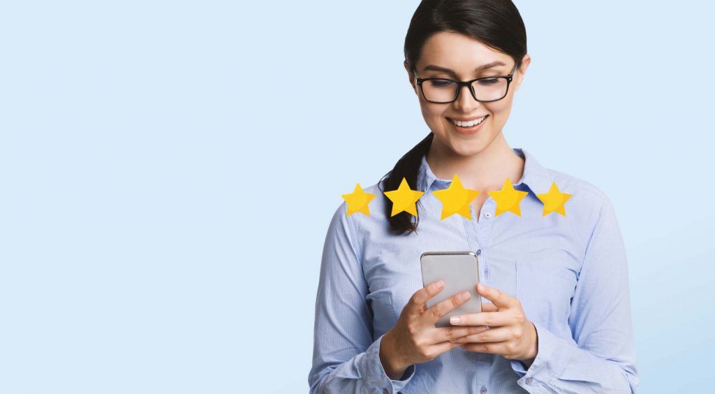 Smiling woman with glasses using her phone, leaving a 5-star review on a light blue background.