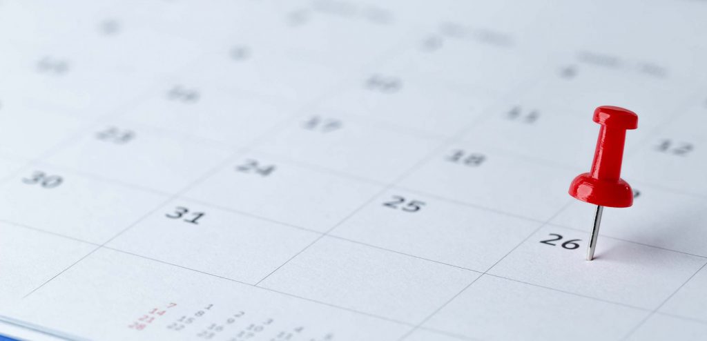 Close-up of a calendar page with a red push pin placed on the 26th, symbolizing an important date or reminder.