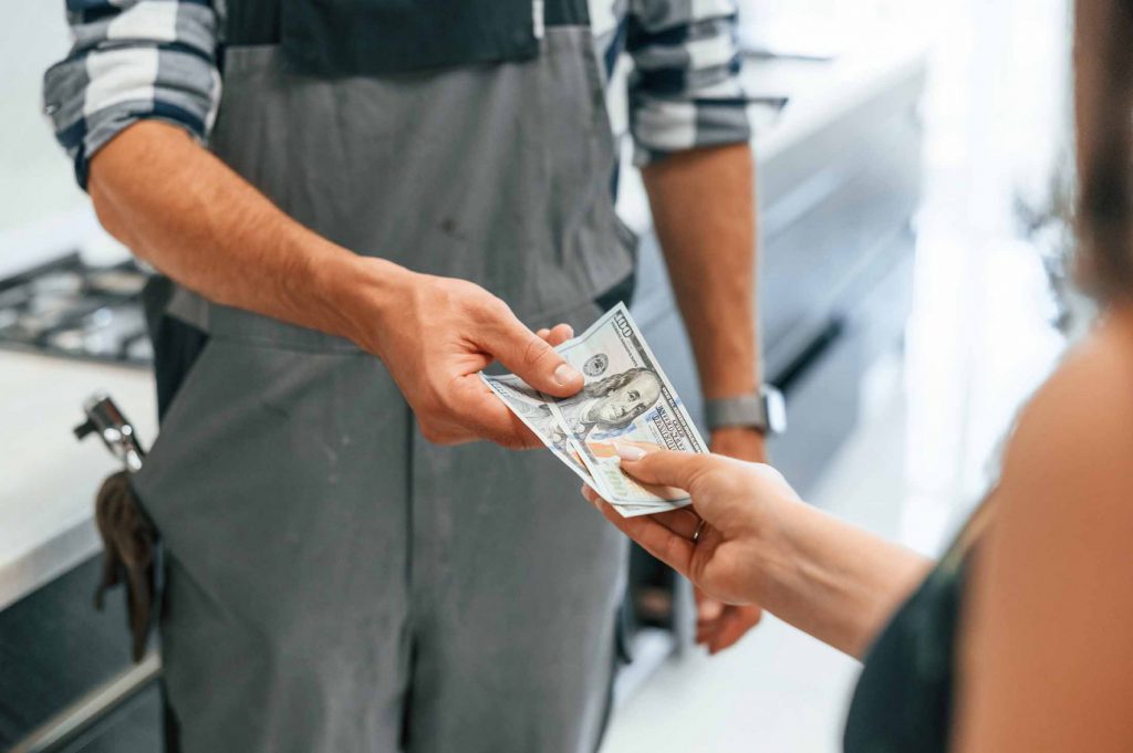 A homeowner paying a plumber in cash for installation or repair services.
