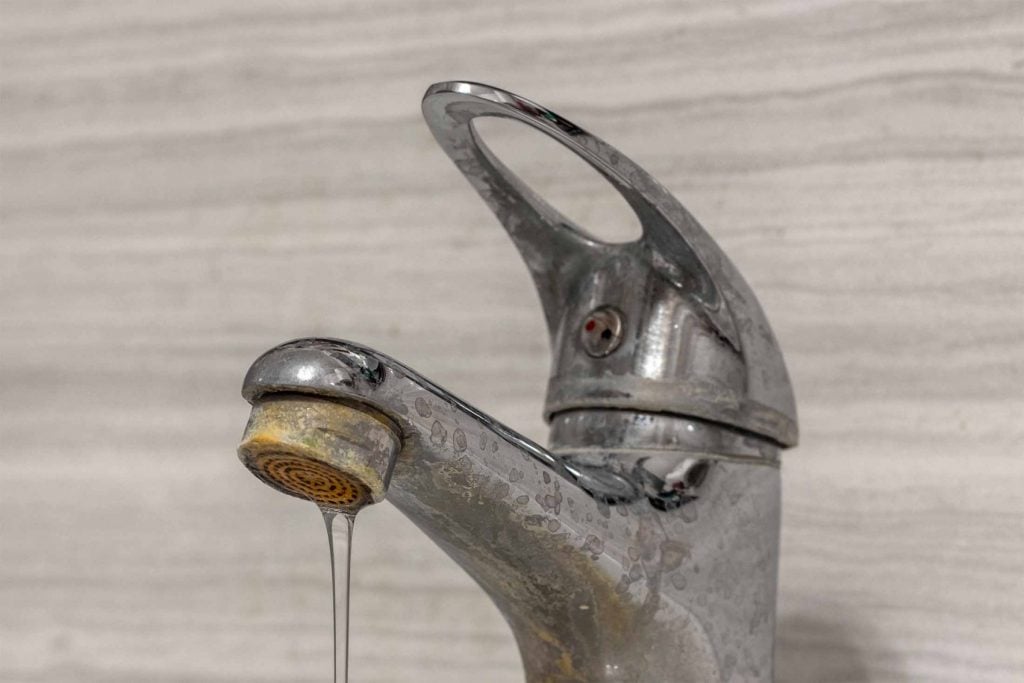 Close-up of a bathroom faucet with mineral buildup and stains caused by hard well water.