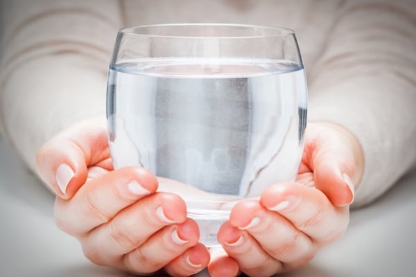 Person holding a clear glass of clean, filtered drinking water, symbolizing safe and healthy water from a home filtration system.