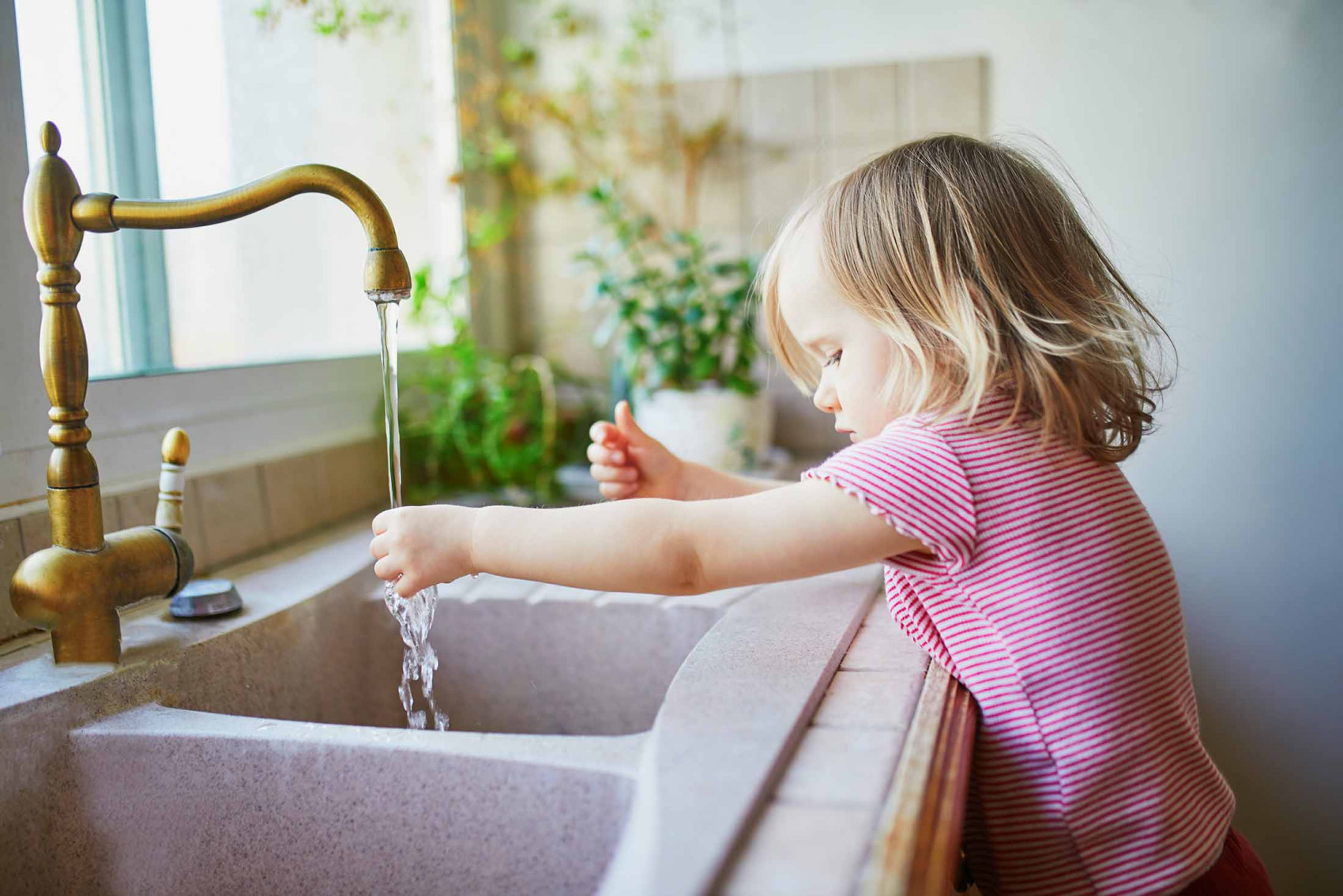 Young child standing at a kitchen sink with running tap water, symbolizing the importance of clean and safe household water.