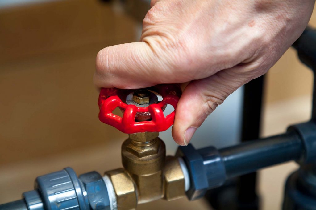 Close-up of a hand turning a red water valve to control water flow in a home filtration system.