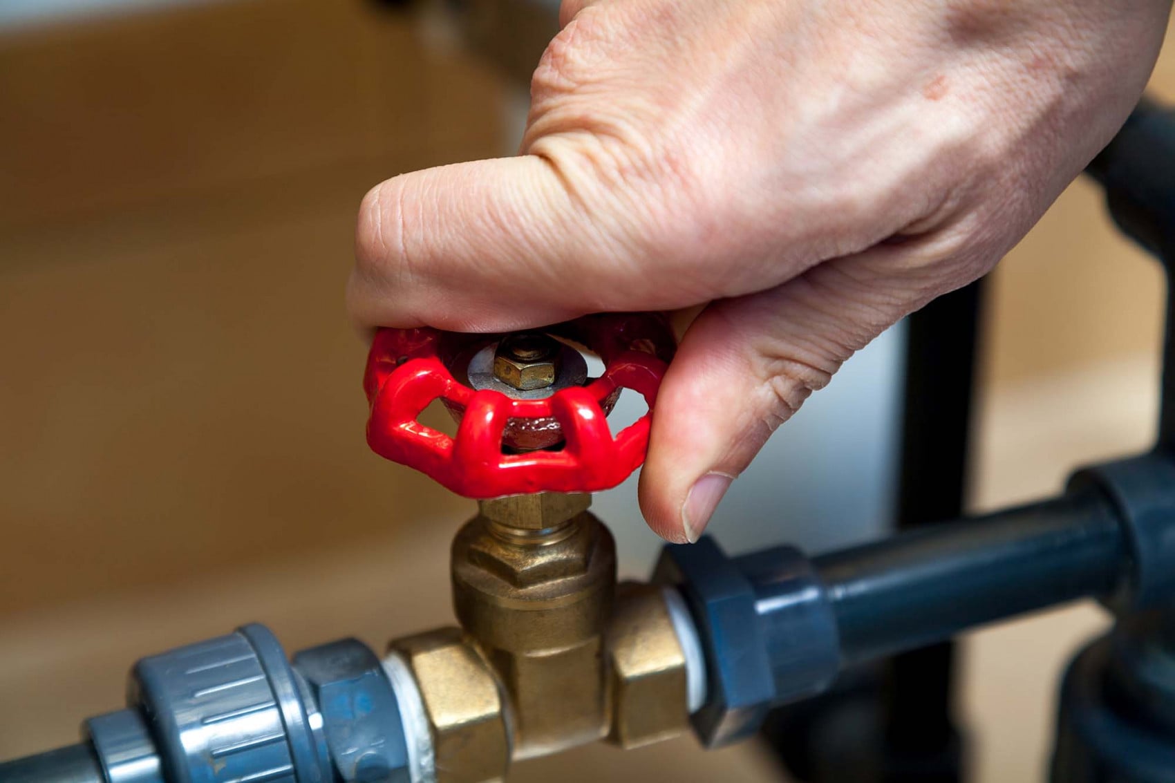 Close-up of a hand turning a red water valve to control water flow in a home filtration system.
