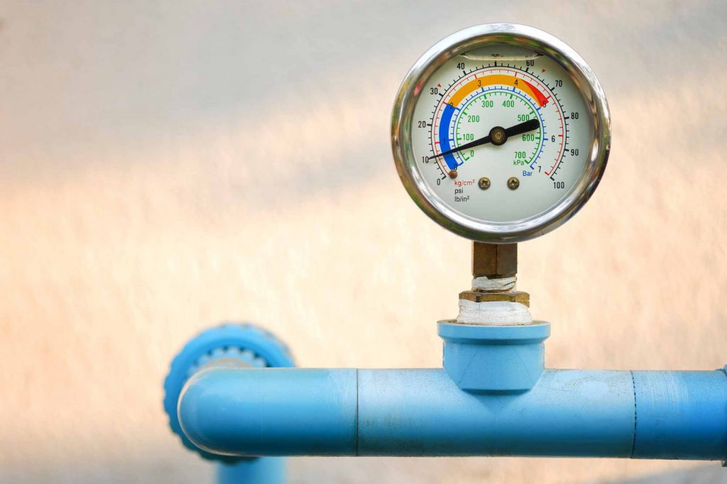 Close-up of a water pressure gauge attached to a blue pipe, used to measure pressure in a home well water or filtration system.