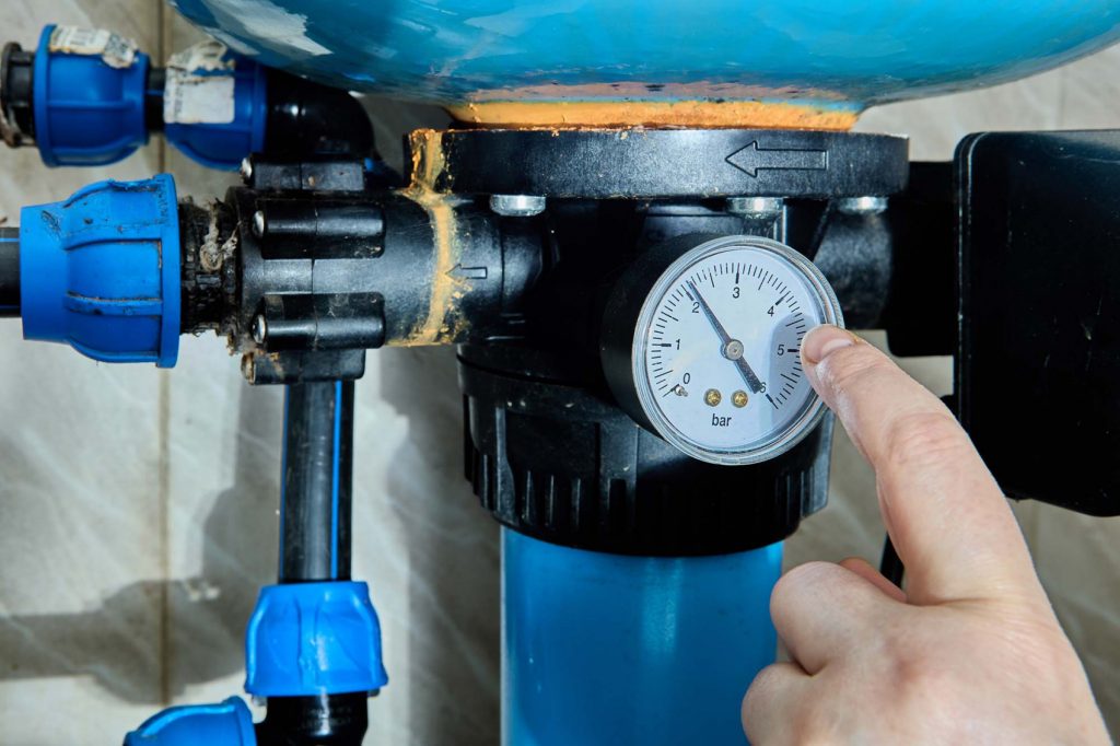 Hand adjusting a well water system pressure gauge to check flow and ensure proper system maintenance and performance.