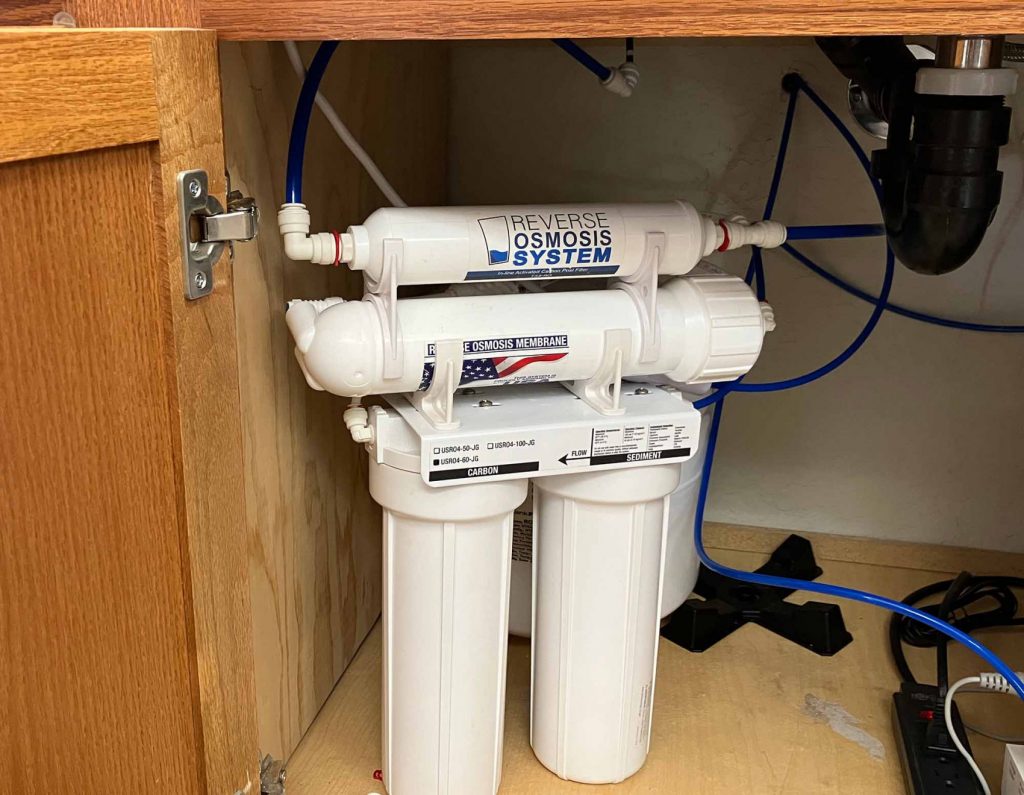Reverse osmosis system installed under a kitchen sink with multiple white filter canisters and blue tubing.