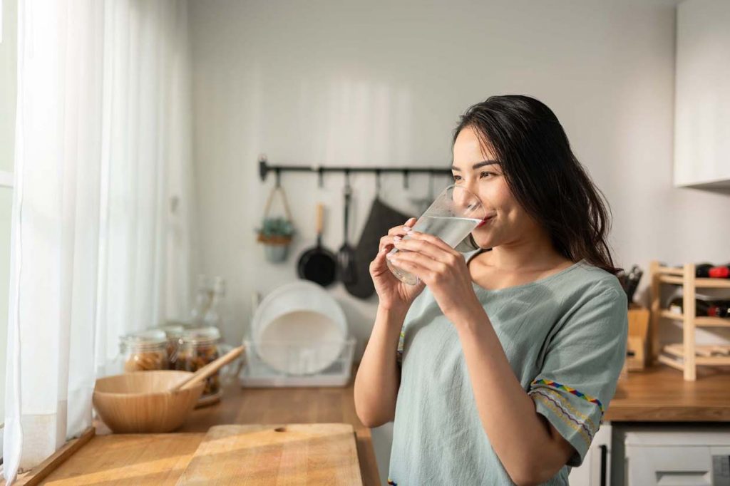 Woman drinking clean filtered well water in her kitchen. 