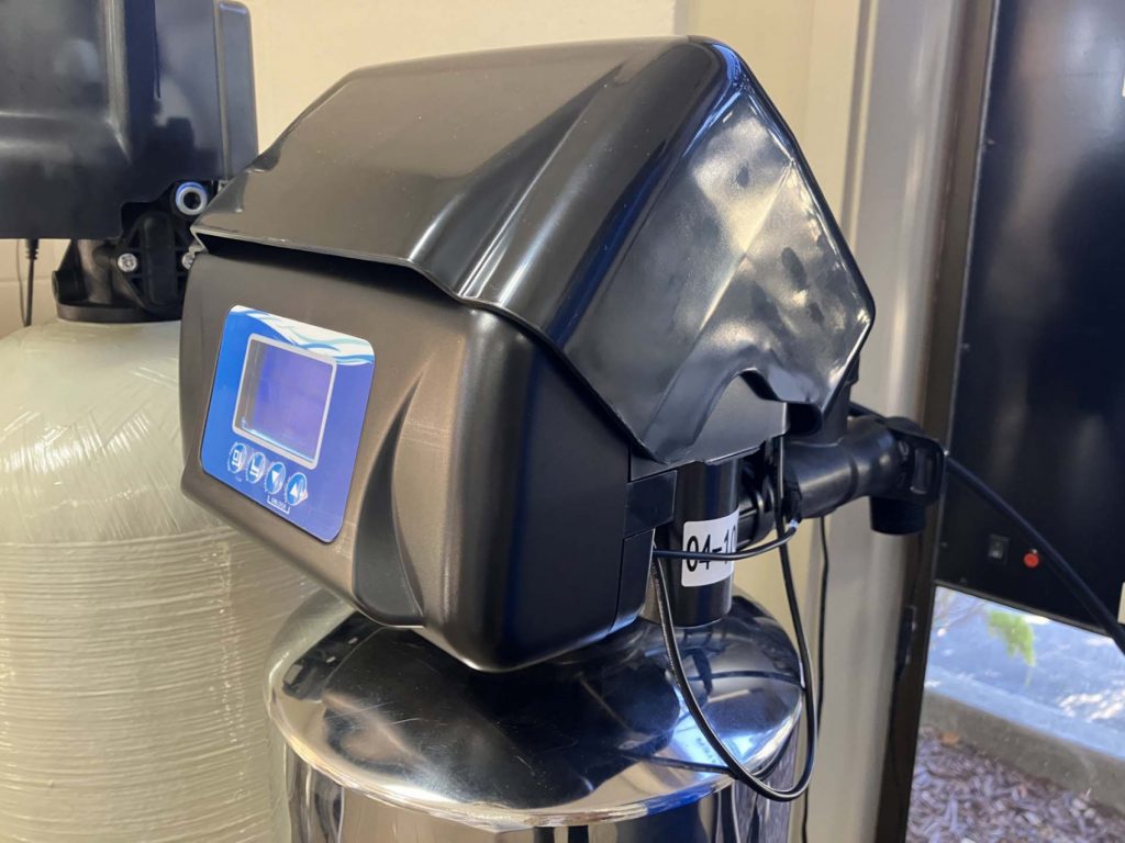 Close-up of a digital control valve mounted on a stainless steel water filtration tank, used to automate backwashing and system settings for whole-house water treatment.
