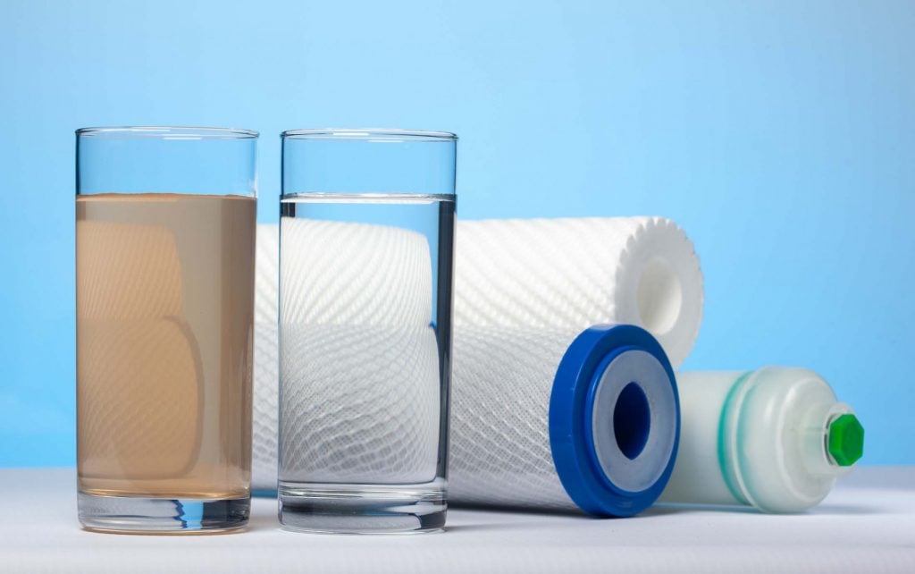 Water Filters and two cups of water, one with sediment and iron and one with filtered water. 