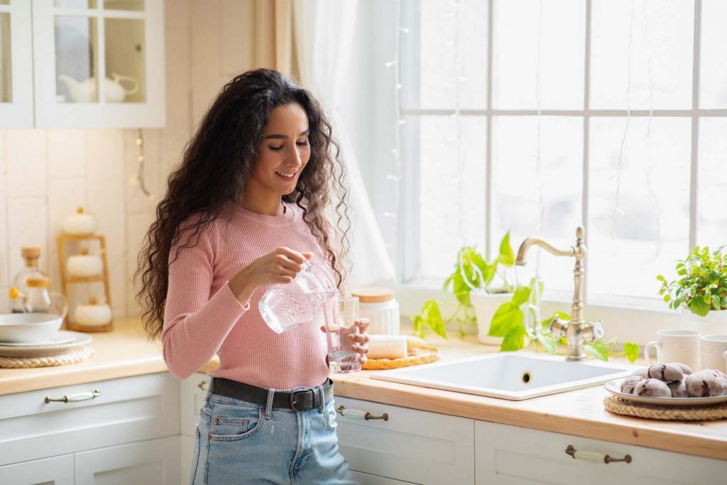 Woman pouring a glass of filtered water in her kitchen.