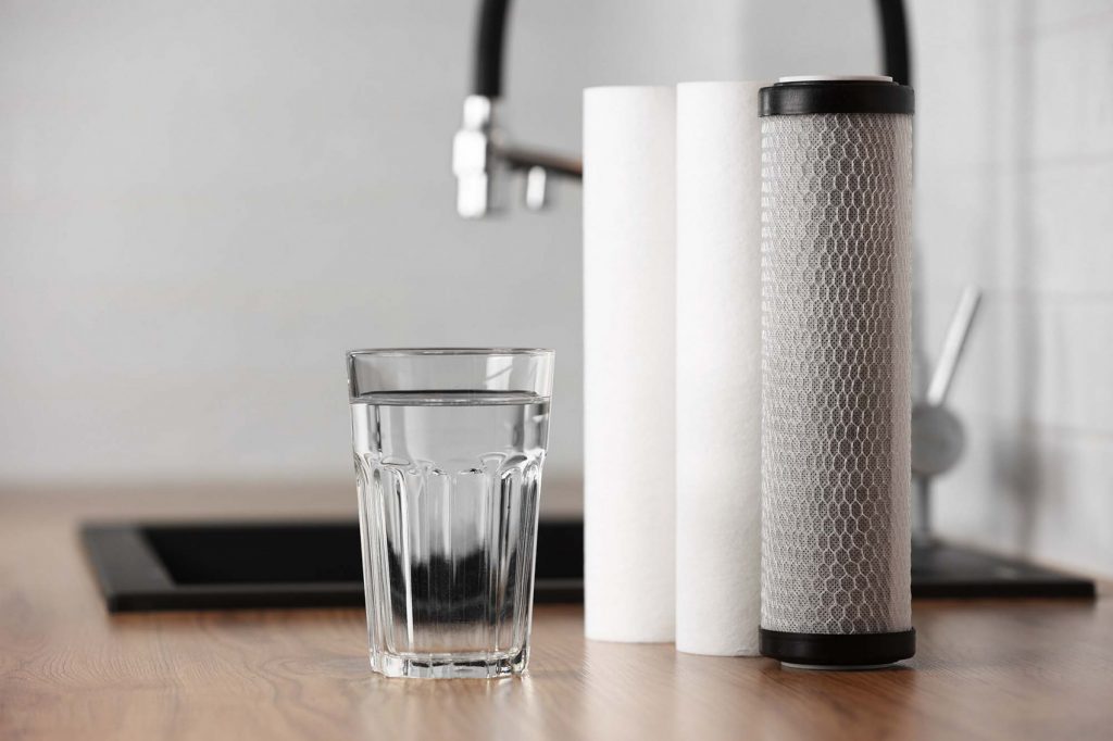 A glass of water next to three water filter cartridges on kitchen counter.