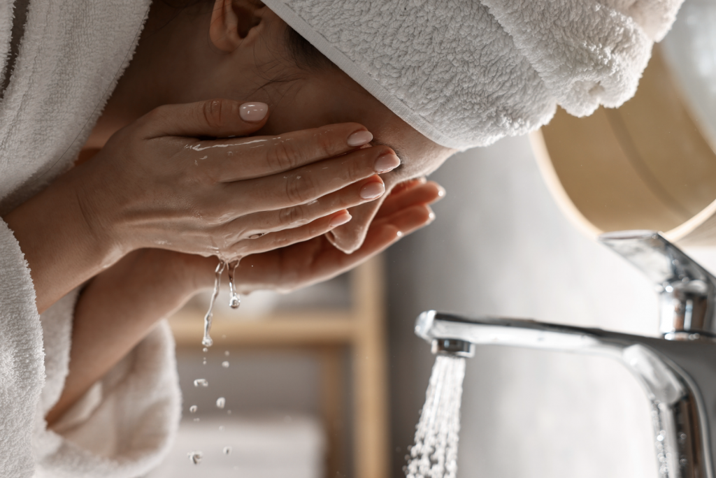 Woman washing her face in bathroom sink.