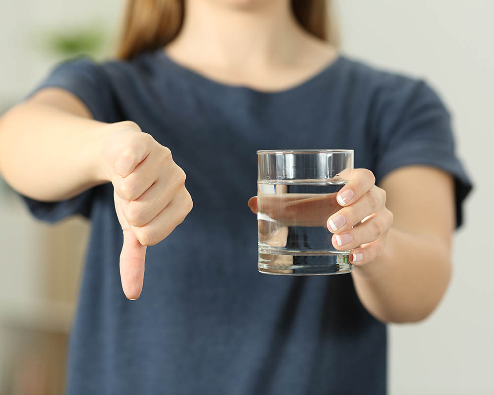 Woman holding a glass of water in one hand and giving a thumbs down with her other hand.