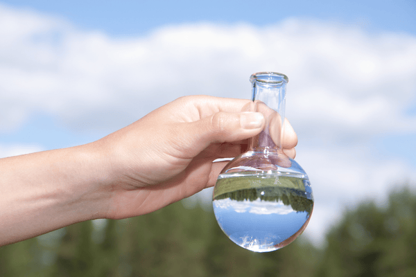 A person holding a glass beaker full of water for the purpose of testing the water.
