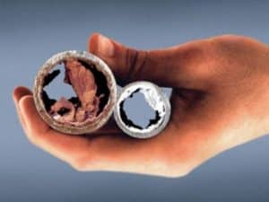 Close-up of a hand holding two corroded metal pipes, showing severe internal scale buildup and corrosion damage caused by poor water chemistry.