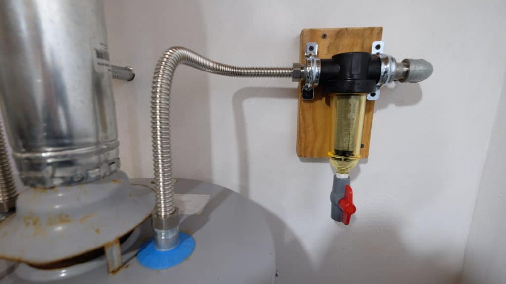 Installed water heater odor killer attached to a hot water tank with flexible metal connectors, designed to eliminate sulfur smells and bacterial odors in hot water systems.