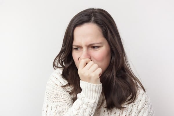 Woman in a white sweater plugging her nose in reaction to an unpleasant odor, representing issues like water heater smells or household odors.